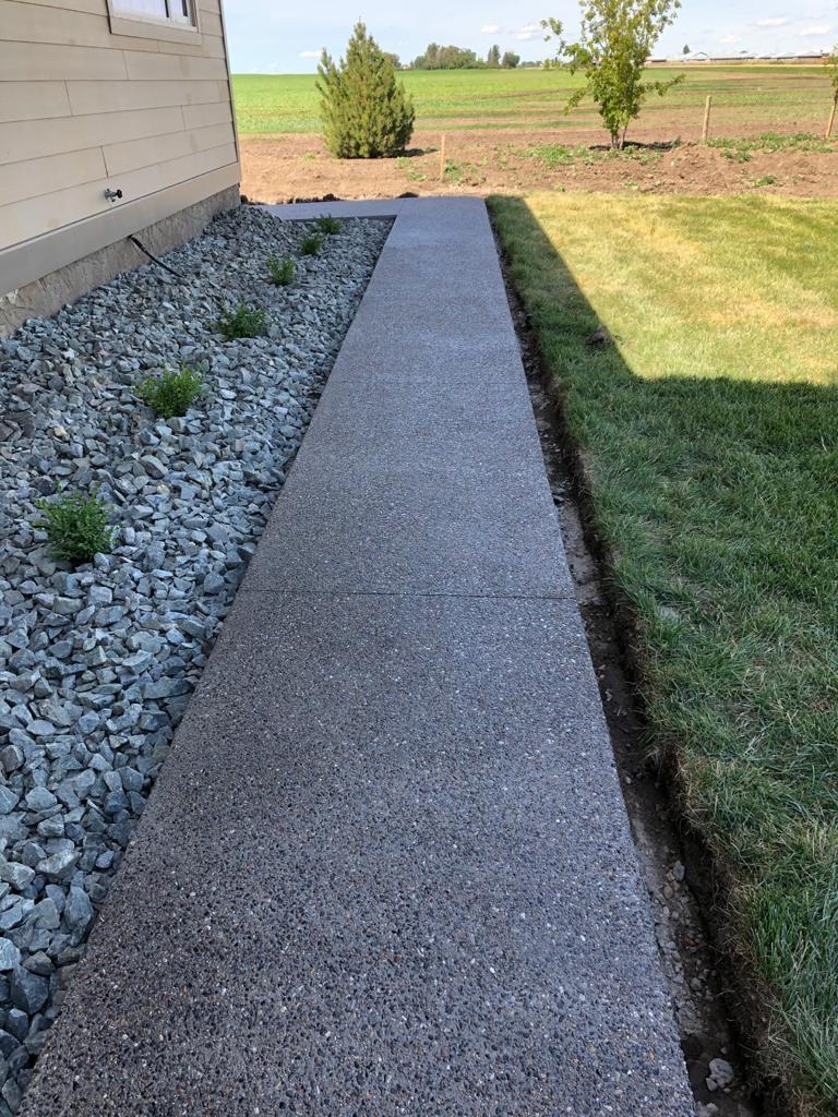 concrete walkway separating grass and a rock bed